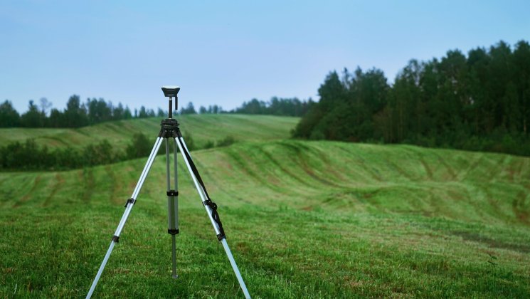 Maamõõtmise kaamera rohelisel põllul. Taamal paistab kuusemets.