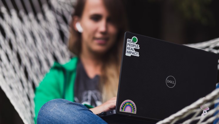 Võrkkiiges istuv rohelises dressipluusis tütarlaps kasutab sülearvutit.