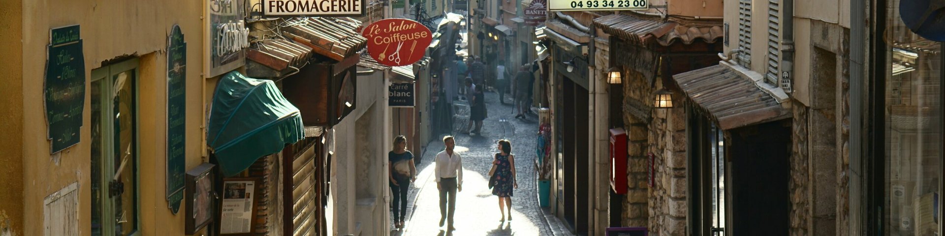 Päikeseline prantsuse väikelinna tänav kolme inimese ja kohvikutega.